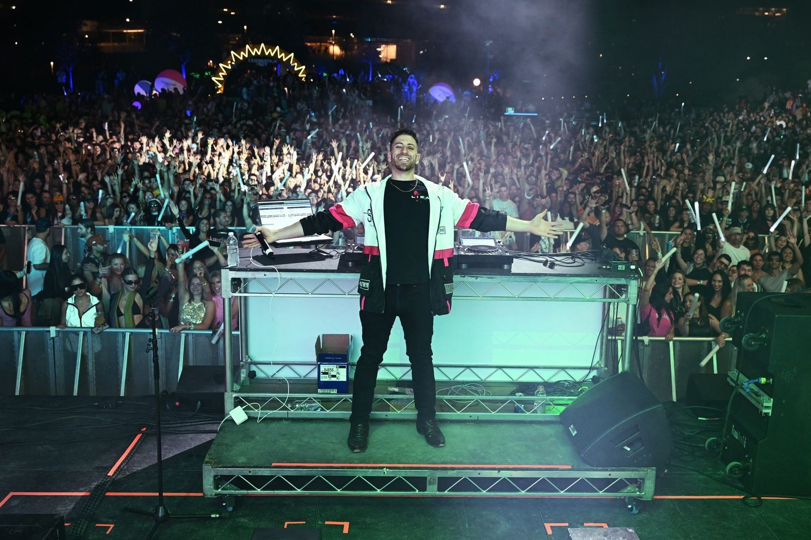 Jordan Miller standing behind the decks with his arms outstretched in front of a large festival crowd.
